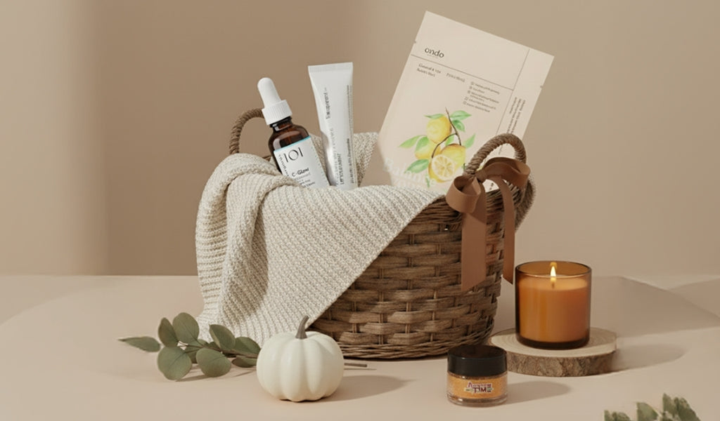 Geschenkkorb mit Hautpflegeprodukten, Decke, Kerze und kleiner weißer Kürbis auf beigem Hintergrund.