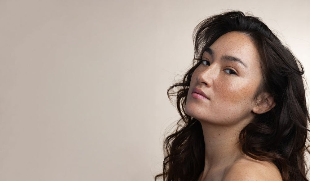 Frau mit braunen langen Haar ohne Make-up vir beigem Hintergrund.