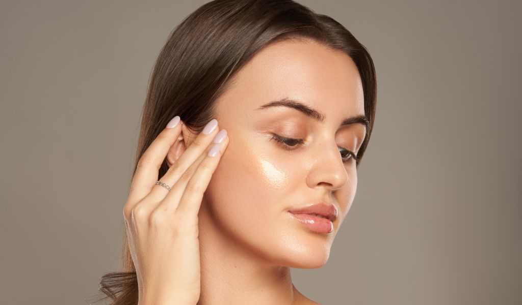 Frau mit glatter Haut trägt Produkt auf die Wange auf und betont ihren natürlichen Glow.