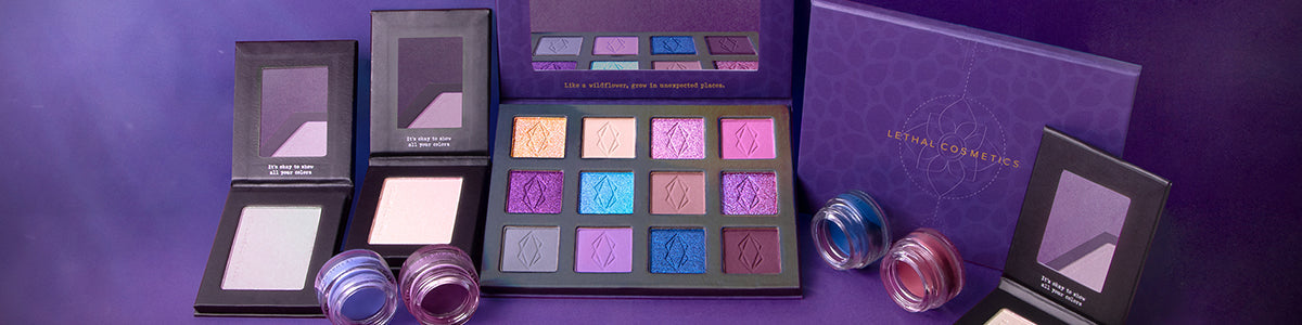 Verschiedene Lidschattenpaletten und Cremelidschatten in Violett- und Blautönen von Lethal Cosmetics vor lila Hintergrund.