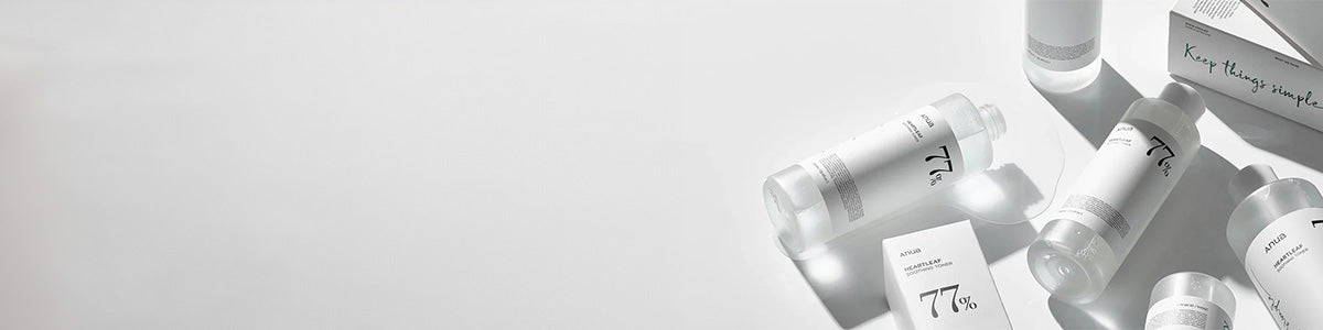 Minimalistische Hautpflegeprodukte in klarer und weißer Verpackung, Flaschen und Schachteln mit der Aufschrift „77 %“ auf hellem Hintergrund.