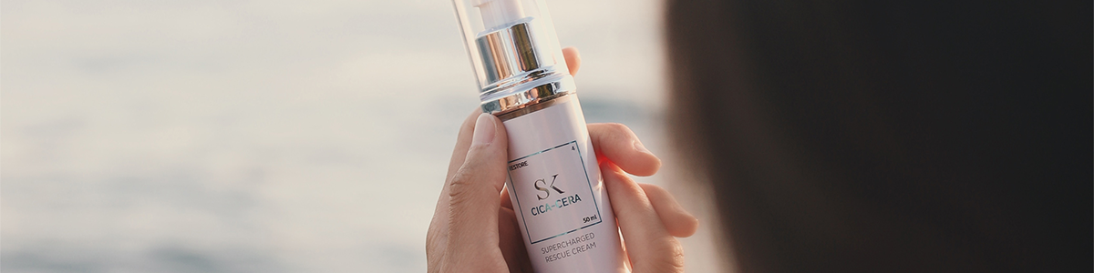 Eine Hand hält eine Serum Flasche vor einem leicht verschwommenen Hintergrund im Freien.