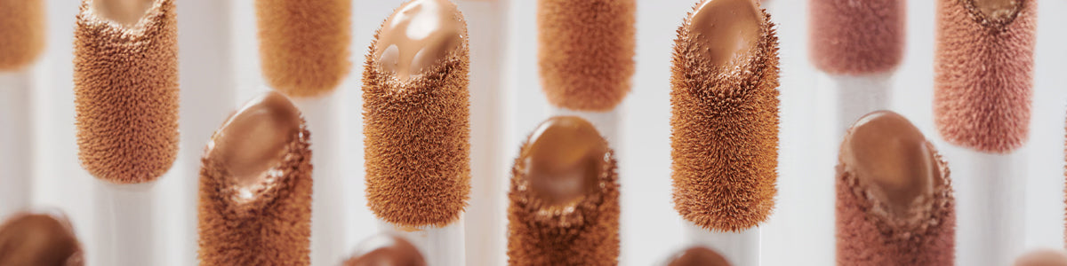 Nahaufnahme mehrerer Concealer-Applikatoren mit unterschiedlichen Farbtönen und flüssigem Concealer an den Spitzen.