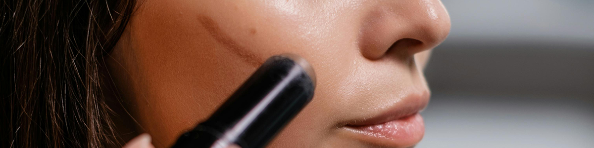 Eine Person trägt einen Kontur-Make-up-Stift auf ihren Wangenknochen auf glatter, reiner Haut auf.
