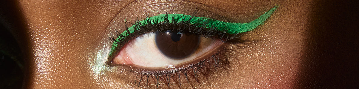 Nahaufnahme eines braunen Auges mit kräftigem grünem Eyeliner und schimmerndem hellgrünem Highlight im inneren Augenwinkel.