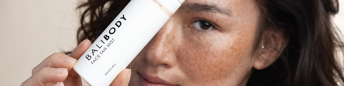 Frau mit Sommersprossen hält eine Flasche Bali Body Face Tan Mist nah an ihr Gesicht und blickt in die Kamera.