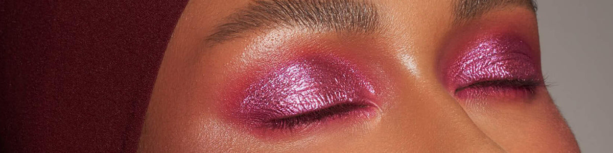 Geschlossene Augen mit kräftigem, glänzendem rosa Lidschatten und gepflegten Augenbrauen, dazu ein weinrotes Kopftuch.
