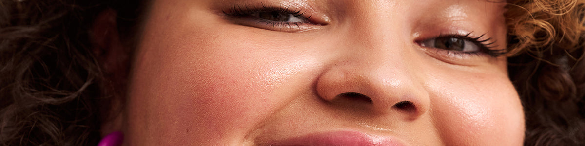 Nahaufnahme einer lächelnden Person mit strahlender Haut, lockigem Haar und dezentem Make-up.