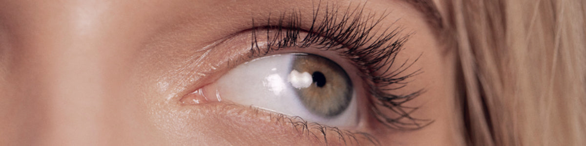 Nahaufnahme des blaugrünen Auges einer Person mit langen Wimpern, die nach oben blickt.