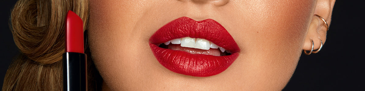 Nahaufnahme des Gesichts einer Frau mit kräftigem roten Lippenstift und einem dazu passenden roten Lippenstift in der Nähe ihrer Lippen.