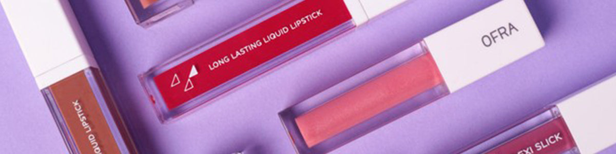 Verschiedene flüssige Liquid Lipsticks in rechteckigen Behältern, angeordnet auf violettem Hintergrund.