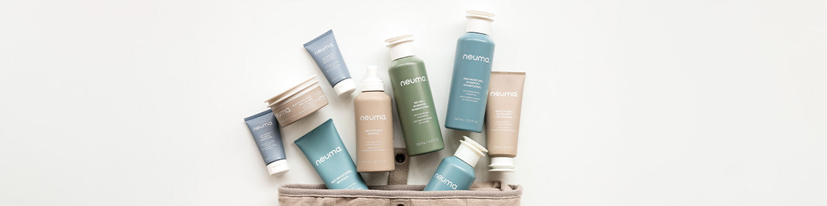 Verschiedene NEUMA Haarpflegeprodukte in Tuben und Flaschen angeordnet über einem beigen Beutel auf weißem Hintergrund.
