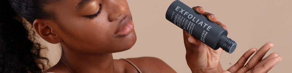 Frau schaut mit entspanntem Blick auf ihre Handfläche, während sie ein flüssiges Peeling-Produkt mit der Aufschrift „Exfoliate“ aufträgt.