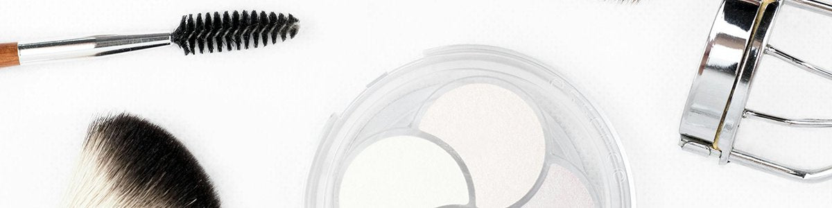 Ausschnitt verschiedener Beauty-Tools auf weißem Hintergrund, darunter Wimpernbürstchen, Fächerpinsel, Lidschattenpalette und Wimpernzange.