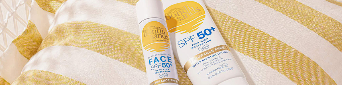 Zwei Sonnenschutzflaschen von Bondi Sands SPF 50+ auf einem gelb-weiß gestreiften Kissen.