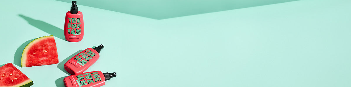 Drei pinke Flaschen mit ‚The Fox Tan‘-Label und zwei Wassermelonenstücke auf türkisfarbenem Untergrund.