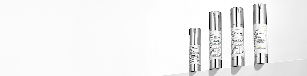 Vier weiße Hautpflegeflaschen mit silbernen Verschlüssen sind in einer Reihe auf einer weißen Fläche vor einem hellen Hintergrund angeordnet.