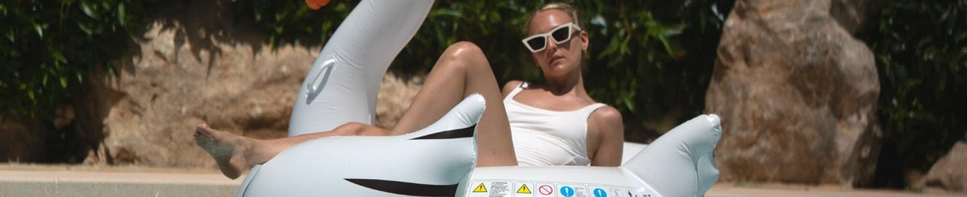 Frau in weißem Badeanzug und Sonnenbrille entspannt auf einem weißen Schwan-Schwimmreifen am Pool