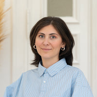 Porträt von Gülsah mit dunkelbraunen Haaren, silbernem Schmuck und hellblauer Bluse vor hellem Hintergrund.