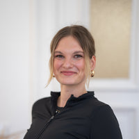 Porträt von Luisa mit dunkelblonden Haaren, braunen Augen und schwarzem Oberteil vor hellem Hintergrund.