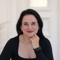 Porträt von Jennifer mit schwarzen Haaren, blauen Augen und schwarzem Oberteil vor hellem Hintergrund.