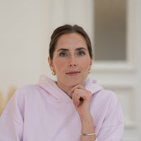 Porträt von Ronja mit braunen Haaren, blauen Augen und rosanem Oberteil vor hellem Hintergrund.