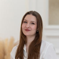 Porträt von Lucie mit braunen Haaren, braunen Augen und weißer Bluse vor hellem Hintergrund.