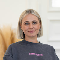 Porträt von Belinda mit platinblondem Haar, blauen Augen und grauem Oberteil vor hellem Hintergrund.