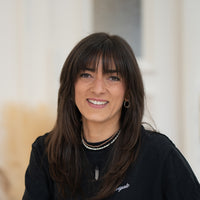 Porträt von Viktoria mit dunkelbraunen Haaren, braunen Augen und schwarzem Oberteil vor hellem Hintergrund.
