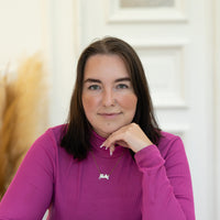 Porträt von Melanie mit dunkelbraunen Haaren und violettem Rollkragenoberteil vor hellem Hintergrund.