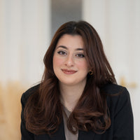 Porträt von Nirang mit braunen Haaren, braunen Augen und schwarzem Blazer vor hellem Hintergrund.