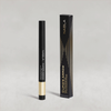 Schwarzer Lidschatten-Stift mit goldener Kappe von NABLA neben der passenden schwarzen Umverpackung mit goldenen Designelementen auf hellem Hintergrund.