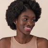 Eine lächelnde Person mit lockigem Haar und dunkler Haut präsentiert das Glossin‘ Glow Tinted Lip Oil 020.