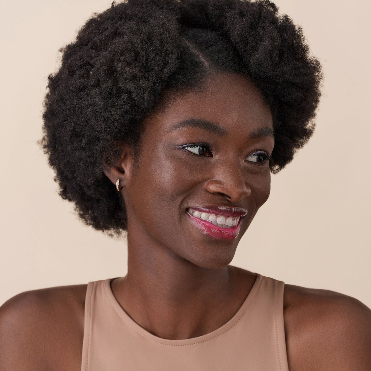 Eine lächelnde Person mit lockigem Haar und dunkler Haut präsentiert das Glossin‘ Glow Tinted Lip Oil 020.