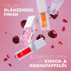 Mehrere Catrice Glossin’ Glow Lip Oils in verschiedenen Farben schweben vor rosa Hintergrund mit Kirschen und Granatapfelkernen – für glänzende, gepflegte Lippen.
