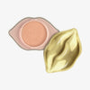 Der KISS & GLOW Shimmer Lip Balm C01 in einem geöffneten lippenförmigen Behälter mit goldenem Deckel und gibt den Blick auf seinen pfirsichfarbenen Lip Balm frei.