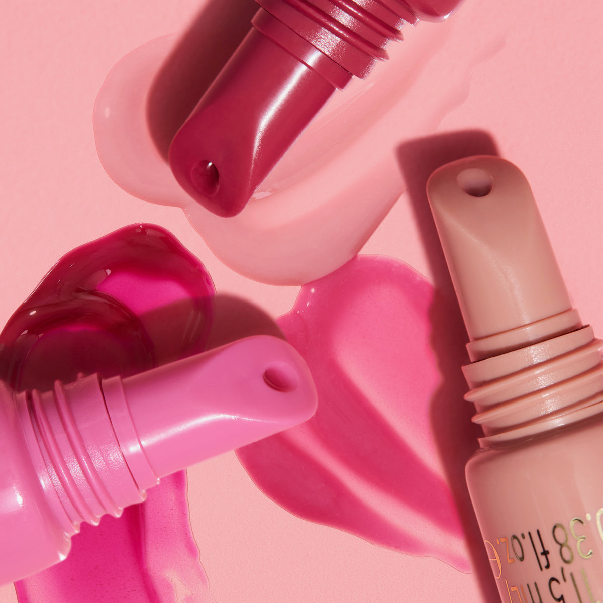 Nahaufnahme der Applikatoren dreier Tuben KISS & GLOW Peptide Lip Tint auf hellrosa Hintergrund.