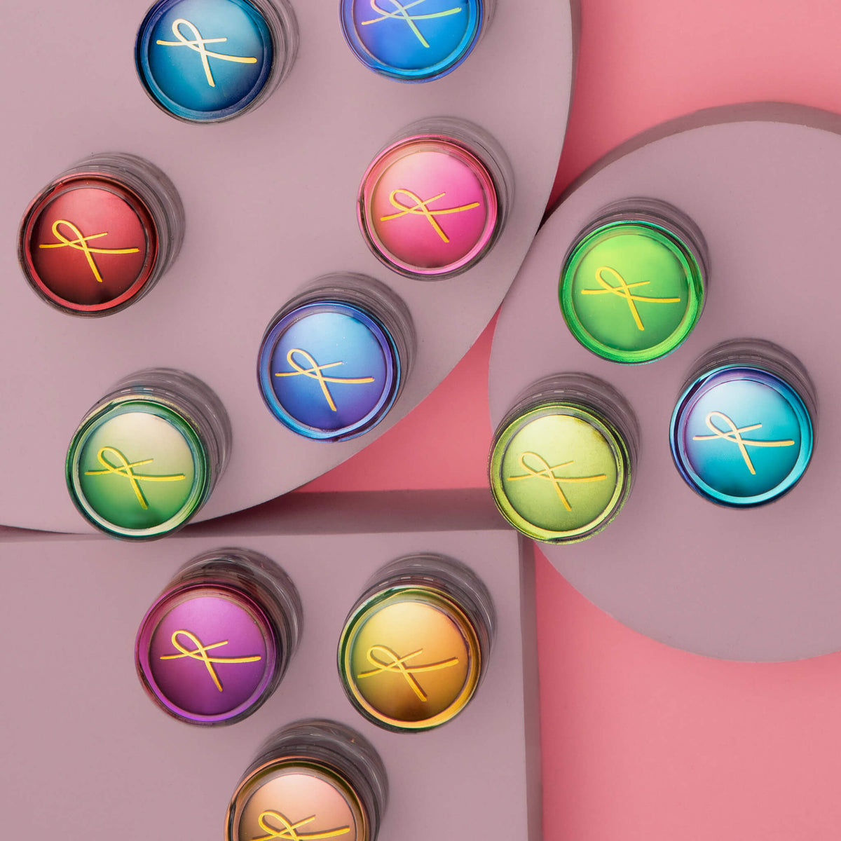 Mehere bunte Tiegel des Karla Cosmetics Original Multichrome Loose Eyeshadow auf geometrischen Formen auf rosa Hintergrund.