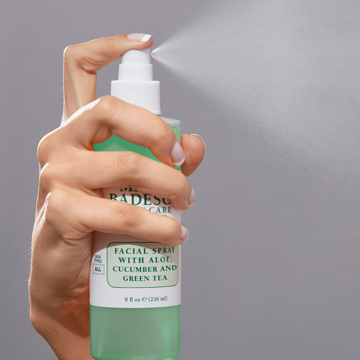 Hand sprüht das Mario Badescu Facial Spray mit Aloe, Gurke und grünem Tee aus einer grünen Flasche .