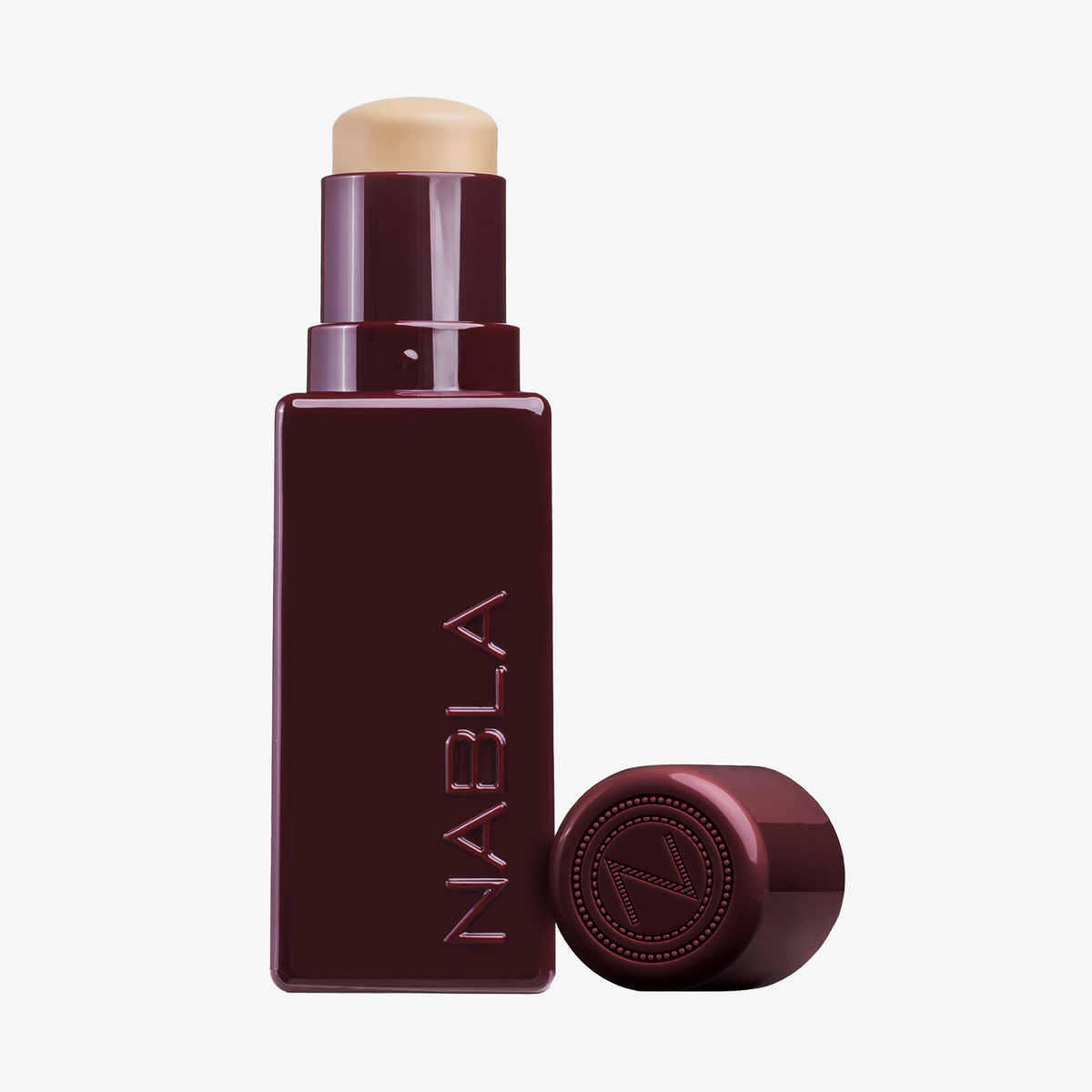 Ein NABLA Cosmetics Art Of Skin Foundation Stick in Burgunderrot, ohne Kappe, steht aufrecht auf weißem Hintergrund.