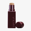 Eine burgunderfarbene Tube NABLA Cosmetics Art Of Skin Foundation Stick mit abgenommener Kappe, die daneben gelegt wird.