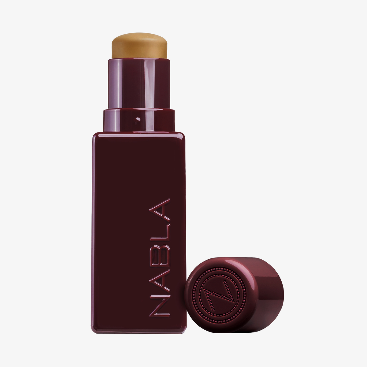 Eine burgunderfarbene, quadratische Tube des NABLA Cosmetics Art Of Skin Foundation Stick ist mit abgenommener Kappe abgebildet, die das beigefarbene Produkt im Inneren offenbart.