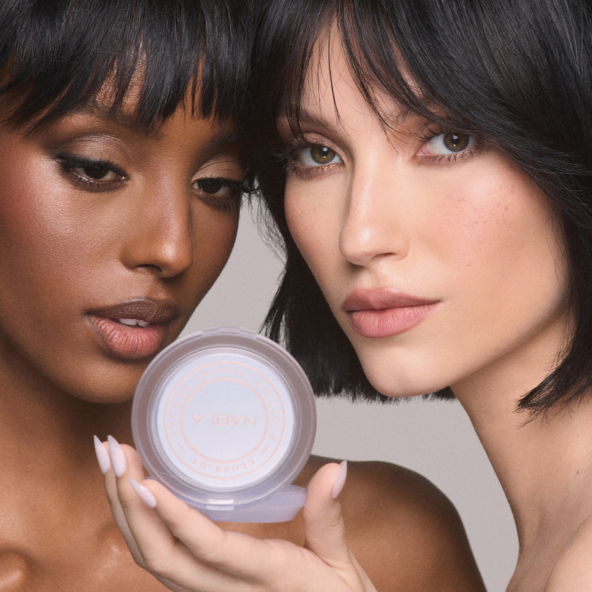 Zwei geschminkte Frauen halten ein Close-up Blotting Pressed Powder Compact und schauen direkt in die Kamera.