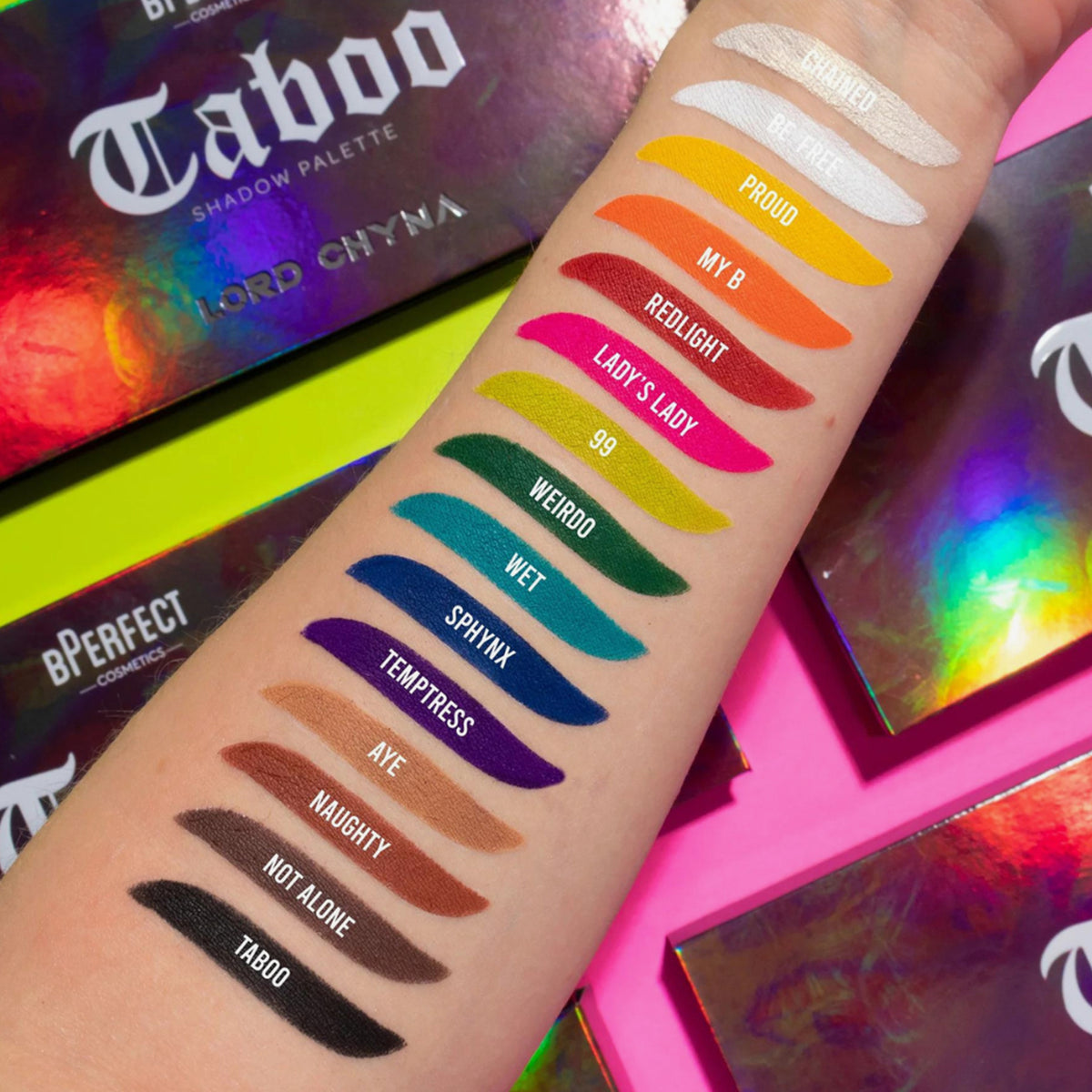 Arm mit farbenfrohen Farbmustern aus der BPerfect Cosmetics x Lord Chyna Taboo Shadow Palette; dahinter Verpackungen