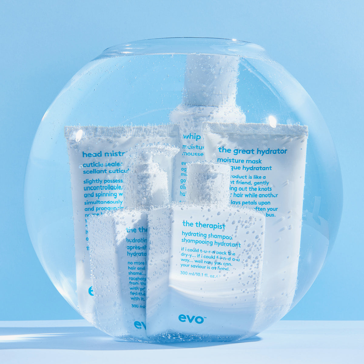 Mehrere Produkte von Evo in einem Goldfischglas mit sprudelndem Wasser vor blauem Hintergrund; darunter das The Therapist Hydrating Shampoo.