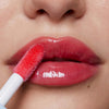 Nahaufnahme voller Lippen, auf die Plumpy Lip Gloss Cherry Red in glänzendem Rosarot aufgetragen wird.