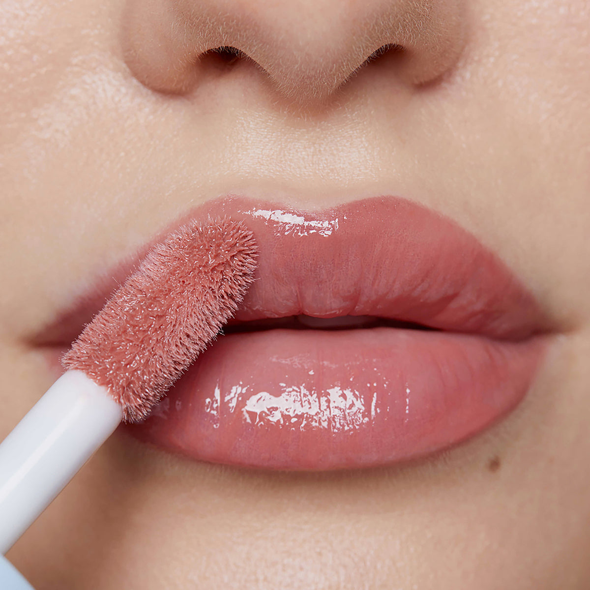 Nahaufnahme voller Lippen, auf die Plumpy Lip Gloss Rose Nude in glänzendem Rosé aufgetragen wird.
