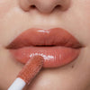 Nahaufnahme voller Lippen, auf die Plumpy Lip Gloss Toffee Brown in glänzendem Pfirsichton aufgetragen wird.