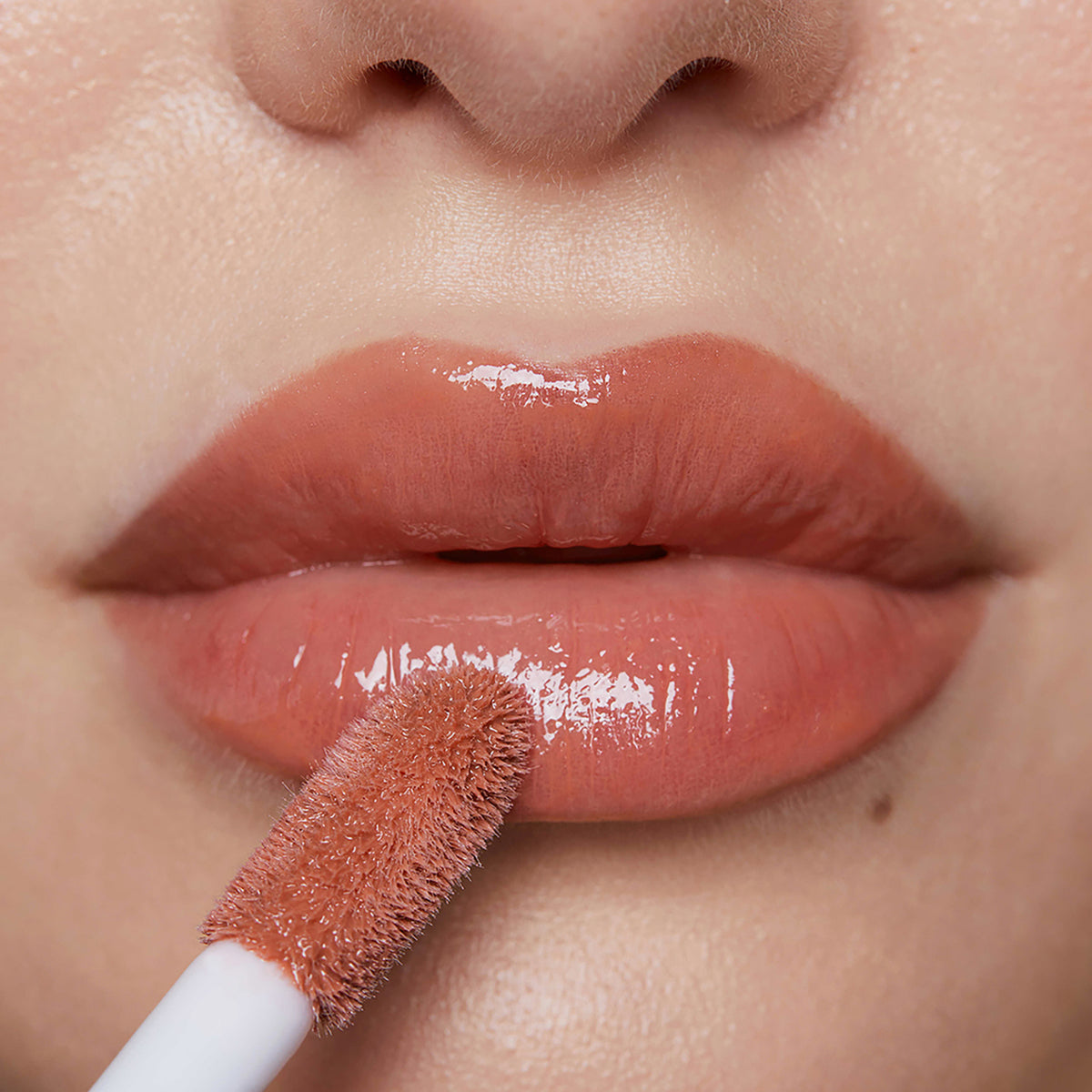 Nahaufnahme voller Lippen, auf die Plumpy Lip Gloss Toffee Brown in glänzendem Pfirsichton aufgetragen wird.