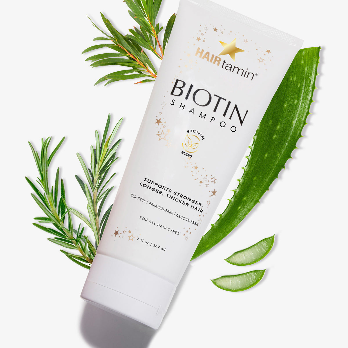 HAIRtamin Biotin-Shampoo-Tube mit daneben angeordneten Rosmarin- und Aloe-Vera-Blättern auf weißem Hintergrund.